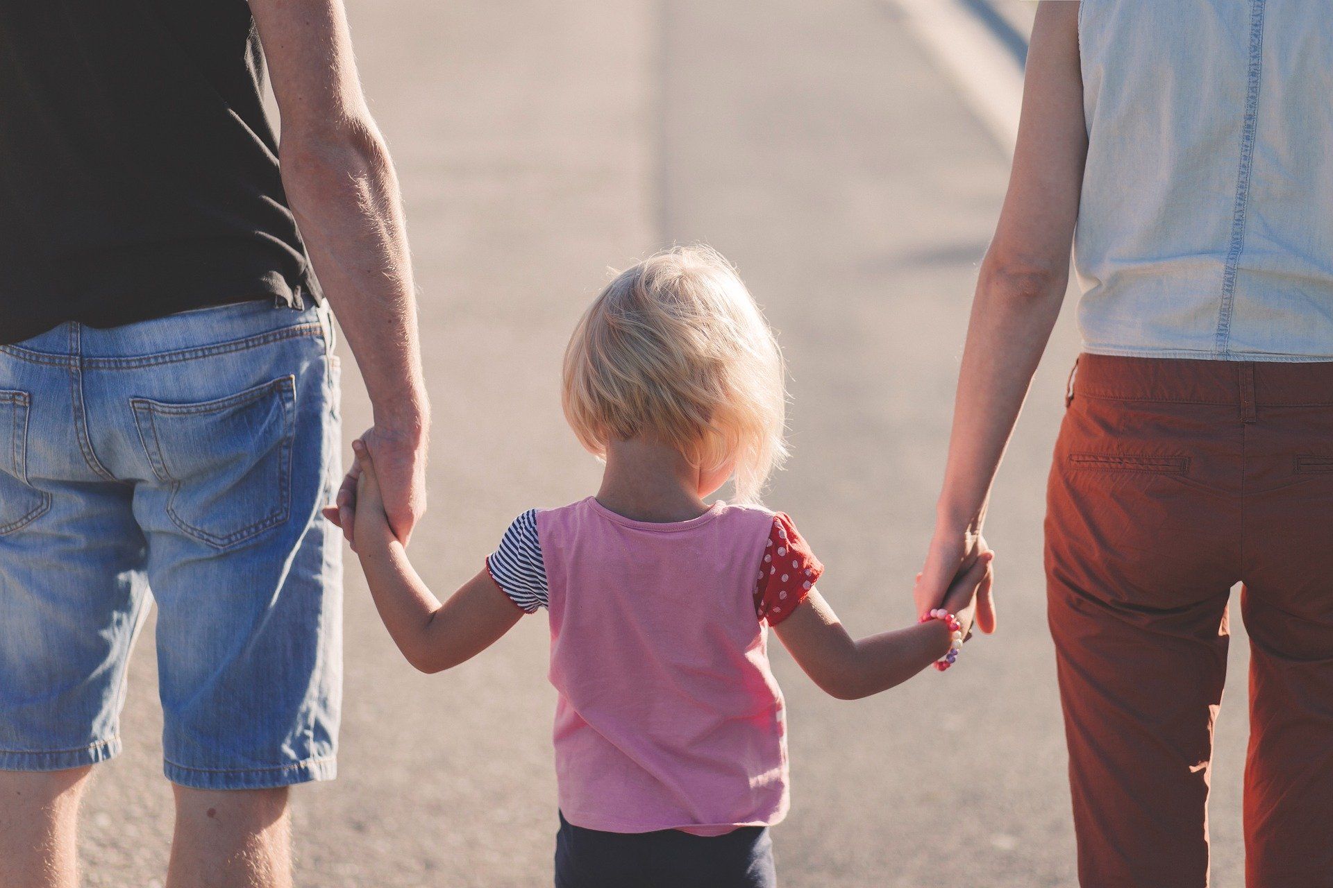 a separated mother and father hold hands with their young daughter who they are co-parenting after divorcing 